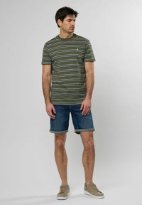 Camiseta verde a rayas de manga corta y escote redondo, combinada con pantalones cortos de mezclilla doblados en los puños y zapatillas beige.