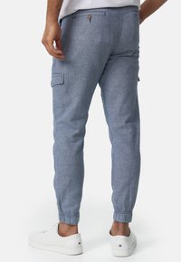 Helle blaue Cargo-Hosen aus strukturiertem Stoff, mit elastischen Bündchen und einer Gesäßtasche mit Knopf. Kombiniert mit weißen Sneakers.