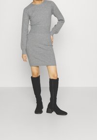 Harmaa ribbineulottu mekko, jossa on pitkät hihat, vartalonmyötäinen vyötärö ja suora helma, yhdistetty mustiin polvipitkiin saappaisiin, joissa on paksut korot.