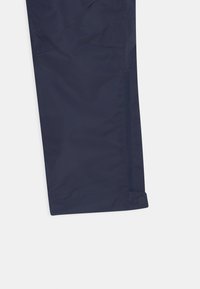 Marinblå vattentäta byxor med en slät yta, med en sidodragskedja och en tryckknappsstängning vid fållen.