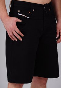 Black denim shorts with a straight cut, featuring copper rivets and a patterned pocket lining. The fabric has a smooth, matte texture.