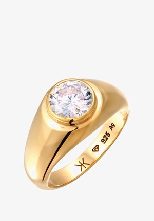 Kuldne sõrmus, mille keskel on suur ümmargune, facettide poolt lihvitud selge kivi. Riba on sile ja poleeritud, läikiva viimistlusega.