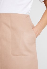 Beige, slät tygkjol med en sidoväska och rena, raka linjer. Midjan sitter i den naturliga midjan.