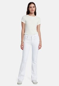Witte flair jeans en een lichtgele t-shirt met korte mouwen. Het t-shirt heeft een kleine, subtiele grafiek op de borst.