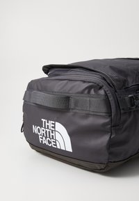 Black fabric backpack with a rectangular shape, featuring The North Face logo in white, zip closure, and durable webbing accents.
