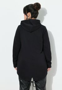Felpa nera a maniche lunghe con cappuccio e cordino sull'orlo, caratterizzata da un retro arrotondato e un tessuto morbido e strutturato. Abbinata a pantaloni neri eleganti.