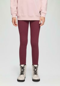 Bordowe legginsy wykonane z elastycznego materiału, zestawione z beżowymi butami na sznurówki z czarnymi sznurówkami i detalem w postaci zamka błyskawicznego z boku.