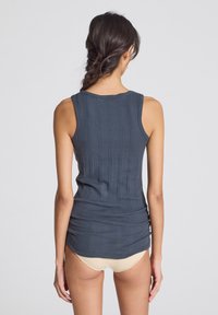 Navy blue ribbed tank top with a fitted design, wide straps, and a scoop neck, featuring vertical texture and slight gathering at the waist.