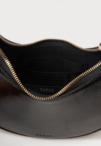 Interno di una borsa a spalla in pelle nera con chiusura a zip, dotata di hardware in tonalità oro, molteplici scomparti per carte e foderato in tessuto con il logo del marchio.
