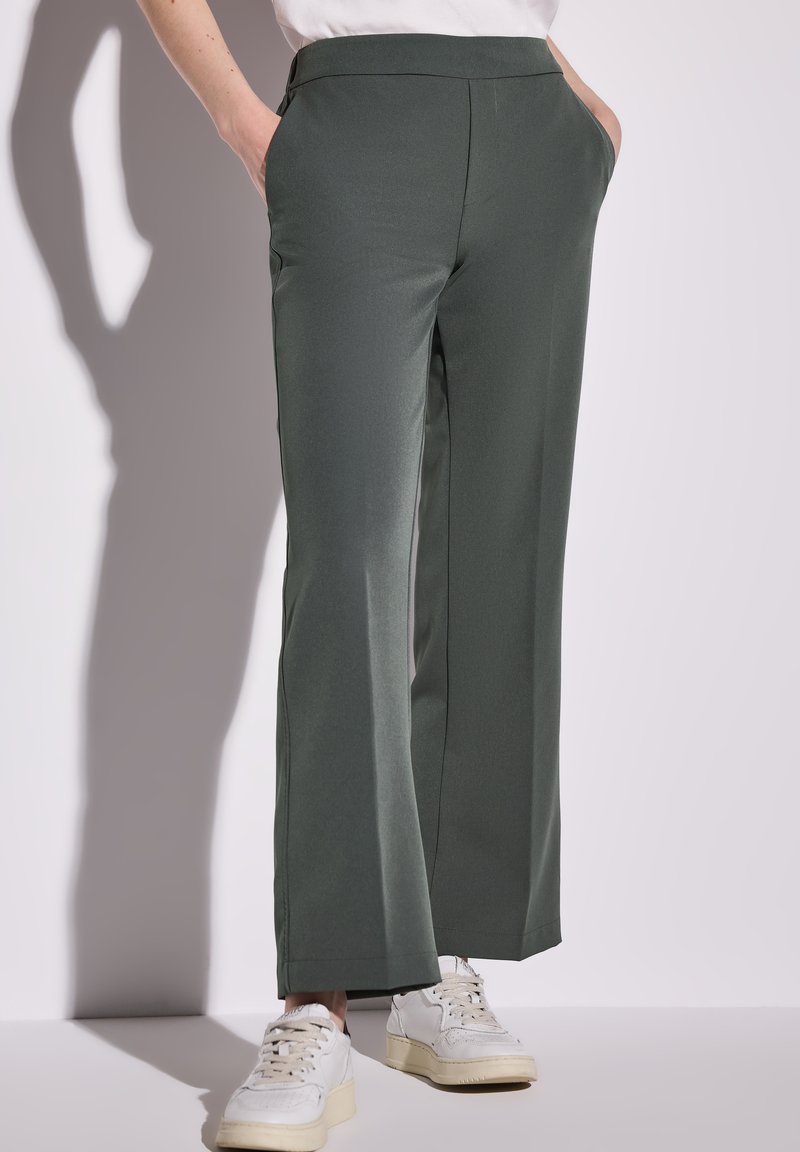 Pantalons larges verts en tissu lisse, dotés de poches latérales et d'une taille épurée, associés à des baskets blanches.