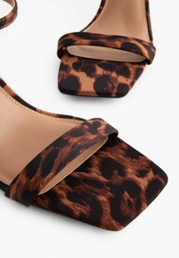 Leopard print aukštakulniai sandalai su kvadratiniu pirštu ir plačia audinio juosta. Medžiaga turi blizgų paviršių ir kreminės spalvos vidinį pamušalą.