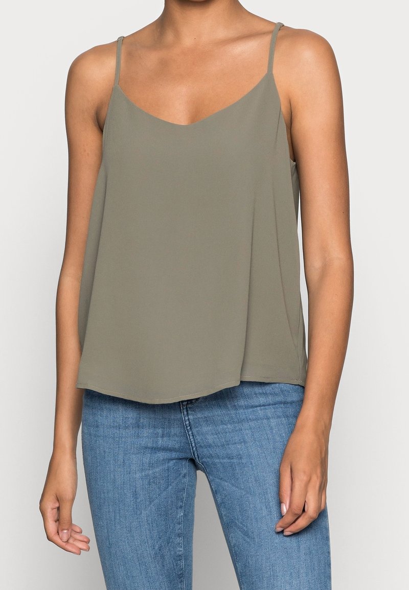Camisole vert olive léger avec des fines bretelles, décolleté en V et un ourlet fluide. Porté avec un jean en denim bleu. Texture douce.