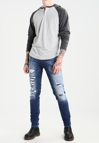 Gray and black long-sleeve henley shirt, paired with distressed blue jeans featuring rips and fading. Black ankle boots complete the outfit.