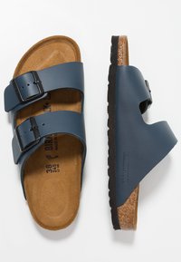 Navyblauwe sandalen met twee banden en zwarte gespen, kurken voetbed en een gestructureerde zwarte buitenzool. Kenmerken zijn de contourvorm en het open ontwerp.