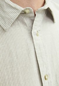 Camicia a maniche corte a righe grigio chiaro con colletto a bottoni e bottoni chiari. Realizzata in tessuto testurizzato con sottili linee verticali.