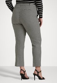 Black and white houndstooth patterned trousers with a fitted design, cropped length, and a back pocket, paired with black high-heeled sandals.
