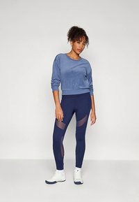 Tumši zila īsa svītrojuma krekls un legingi ar caurspīdīgu paneļu akcentiem. Mīksta tekstūra, pieguļoša forma, un saskaņoti ar baltajām sporta kurpēm.