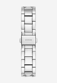 Srebrna kovinska ura z bandem s poliranim zaključkom, z povezanim dizajnom in pravokotnim sponko z vgraviranim imenom blagovne znamke "GUESS".