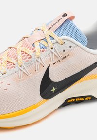 La chaussure de trail running Nike présente un dessus en mesh rose avec des accents bleus, des lacets jaunes et un swoosh noir. Semelle texturée et talon rembourré.