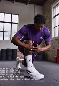 Camiseta deportiva morada de manga corta, zapatillas deportivas blancas y negras, y pantalones cortos negros, arrodillado mientras se estira. Texto superpuesto en varios idiomas.