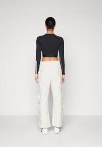 Černý dlouhý rukáv crop top spárovaný s bílými cargo kalhotami. Top má kontrastní boční pruhy; kalhoty mají boční kapsy a volný střih.