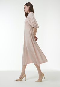 Blassrosa, knielanges Kleid mit Puffärmel, weichem Material und lockerer Passform, kombiniert mit hautfarbenen High Heels.