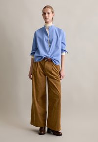 Lichtblauw overhemden met kraag en één zak, gecombineerd met brede, bruine corduroy pants en bruine haklaarzen.