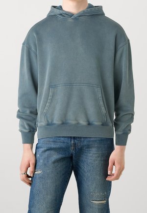Lichtblauwe hoodie van een katoenmix, met een zak aan de voorkant, ribgebreide manchetten en een capuchon met trekkoord. G gedragen met versleten spijkerbroek.