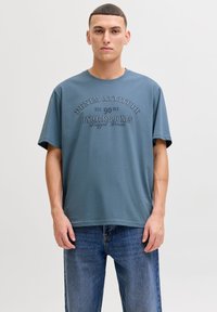 Blue cotton t-shirt with short sleeves and a crew neck, featuring raised text in contrasting color: "DENIM ATTITUDE" and brand name.