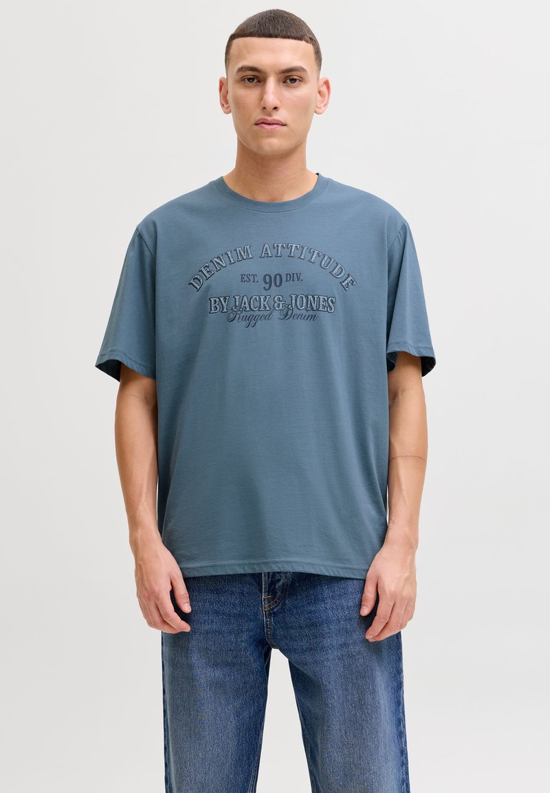 Blue cotton t-shirt with short sleeves and a crew neck, featuring raised text in contrasting color: "DENIM ATTITUDE" and brand name.