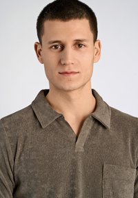 Brun, texturerad pikétröja i mjukt tyg, med en treknappslå och en bröstficka samt en modern kragsdesign.