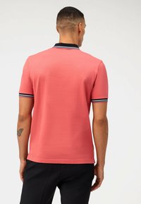 Polo shirt à manches courtes en corail avec un col bleu marine contrastant et des accents rayés. Texture lisse et coupe classique. Vue arrière présentée.