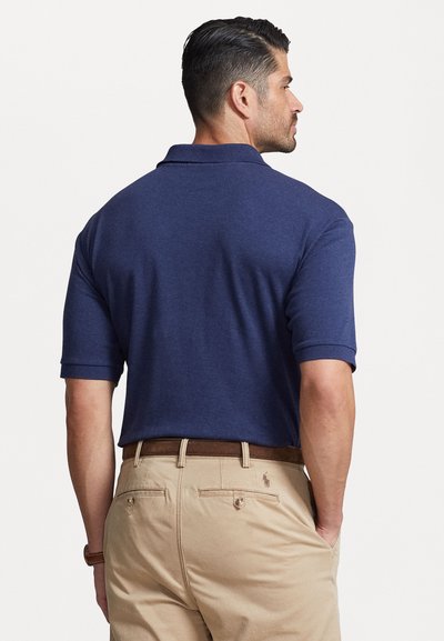 Mørkeblå kortermet polo skjorte laget av myk stoff, med klassisk krage og avslappet passform, kombinert med beige bukser og et brunt belte.