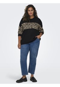 Pulover z leopardjim vzorcem v črno-rjavi barvi s tremi četrtinami rokavov, v kombinaciji s svetlo modrimi naravnost krojenimi džinsom in črnimi loafers.