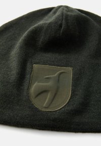 Tmavo zelená čiapka vyrobená z jemnej pleteniny, s textúrovanou olivovo zelenou nášivkou so stylizovaným logom.