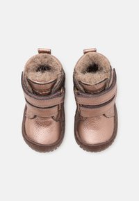 Metalické bronzové boty pro batole s měkkou, huňatou podšívkou a suchými zipy, zobrazené zvrchu na bílém pozadí.