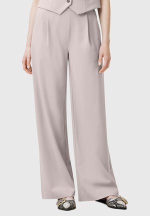 Pantalon beige clair à jambes larges porté avec des chaussures slip-on à imprimé serpent avec de grandes boucles dorées.