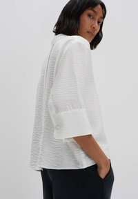 White textured shirt with a collar, three-quarter sleeves, and a loose fit; features subtle sheen and soft fabric with contrasting cuff.