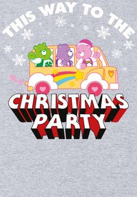 Autobús amarillo con osos de dibujos animados, verde, púrpura y rosa, rodeado de copos de nieve. El texto dice "Este camino hacia la fiesta de Navidad" en rojo negrita.