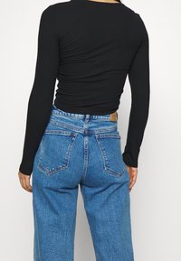 Schwarzes, geripptes Langarmshirt kombiniert mit hoch taillierten, hellblauen Denimjeans. Die Jeans verfügen über klassische Taschen und einen lockeren Schnitt.