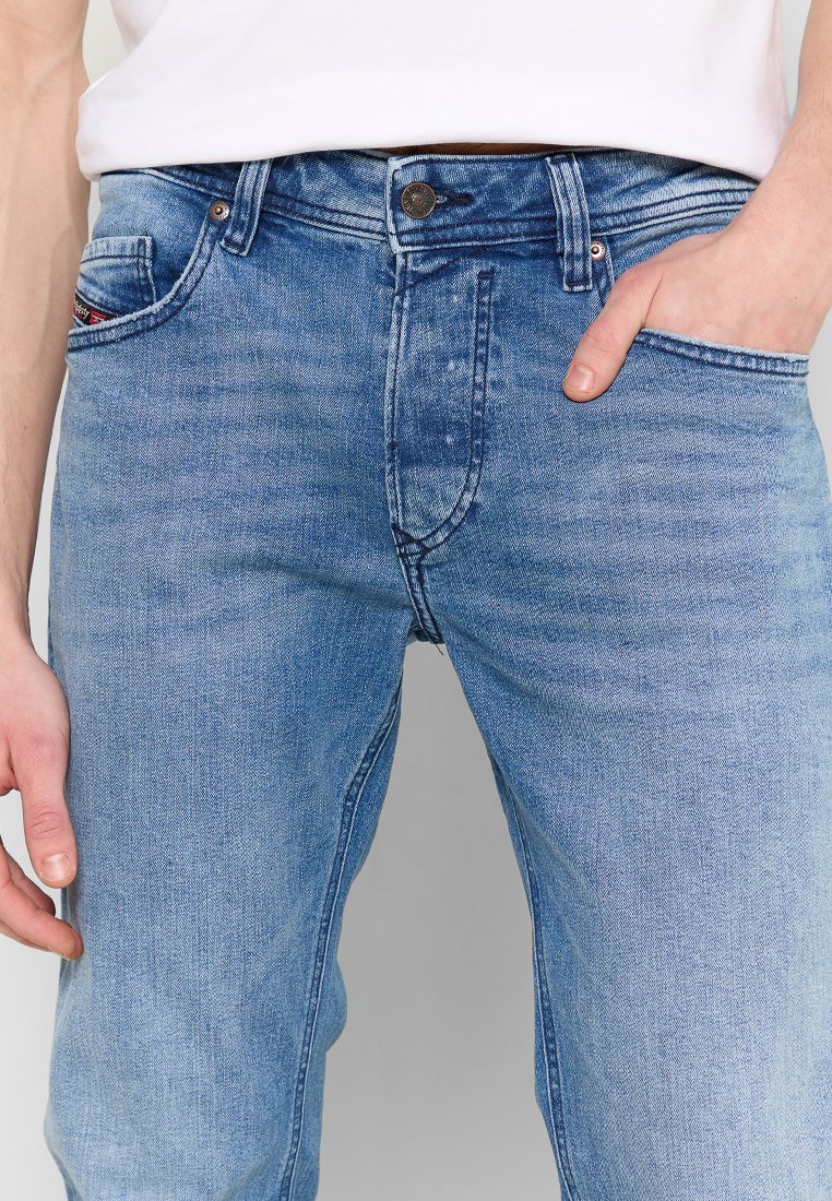 Jean en denim bleu clair avec une finition délavée. Caractéristiques d'un design standard à cinq poches, fermeture à bouton en métal et éléments de couture.
