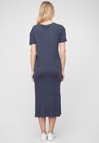 Tengerészkék pólóruha puha anyagból, térdig érő, rövid ujjú, oldalsó hasítékokkal a mozgás megkönnyítésére, fehér tornacipővel párosítva.