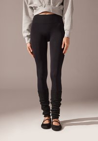 Schwarze Leggings mit einem nahtlosen Bund, kombiniert mit lässigen schwarzen Beinstulpen und einfachen schwarzen Ballerinas. Weicher, dehnbarer Stoff.