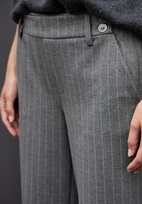 Grau gestreifte Hose aus weichem Stoff, mit geradem Schnitt, Fronttaschen und zwei Metallknöpfen am Bund.