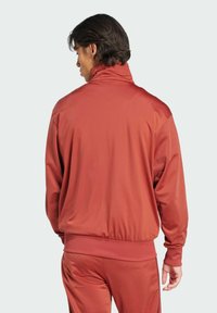 Chaqueta deportiva roja con cuello alto, mangas largas y puños acanalados. Material liso y ligero con un diseño sencillo y sin adornos.