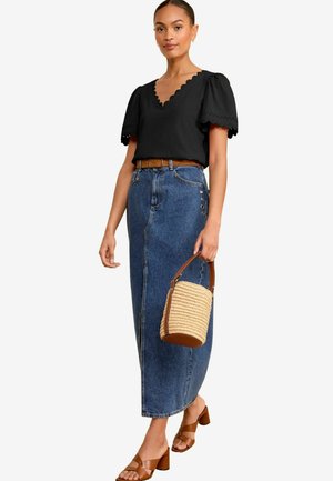 Blusa nera a sottopunto con maniche a sbuffo, gonna in denim a vita alta con dettaglio dei bottoni laterali, cintura marrone e borsa in paglia color tan. Sandali con tacco a blocco marroni.