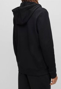 Sweat à capuche noir avec un tissu doux et texturé, une capuche spacieuse, ainsi que des poignets et un ourlet côtelés. Le design est simple et classique.