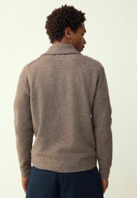 Pruun kootud kampsun allapoole pööratud kraega, pikkade varrukatega ja soonikkoes alläärtega. Tekstuur on pehme ja veidi karvane.