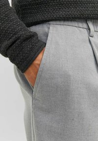 Grå skräddarsydda byxor med en slät yta och klassisk passform, kombinerat med en mörk stickad tröja med ett strukturerat mönster.