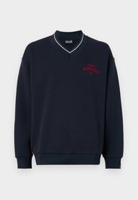 Sweatshirt azul marinho com um design de decote em V. Apresenta um bordado vermelho de "MILANO GYMNASIUM EA7" no peito. Tecido macio e texturizado.